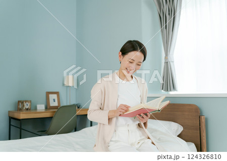 ベッドのそばに座って本を読む女性 124326810