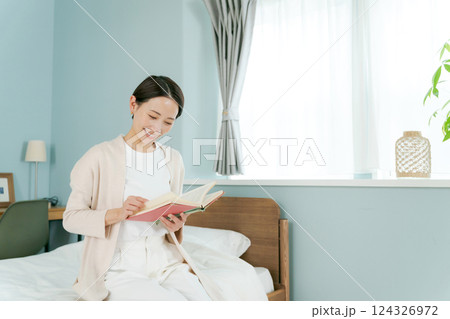 ベッドのそばに座って本を読む女性 124326972