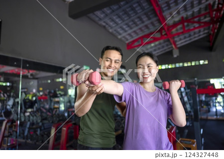 Chinese east asian woman working out lifting a dumbbell with an indonesian southeast asian personal trainer man at the gym. Fitness exercise and healthy lifestyle concept Chinese east asian woman working out lifting a dumbbell with an indonesian southeast asian personal trainer man at the gym. Fitness exercise and healthy lifestyle concept 124327448