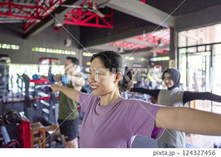 Chinese east asian and Arab middle eastern muslim woman with indonesian southeast asian man working out while stretching and lifting dumbbell at the gym. Fitness exercise and healthy lifestyle concept 124327456