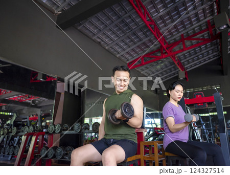 Indonesian southeast asian man and chinese east asian woman working out lifting a dumbbell at the gym. Fitness exercise and healthy lifestyle concept 124327514