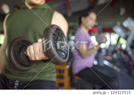 Indonesian southeast asian man and chinese east asian woman working out lifting a dumbbell at the gym. Fitness exercise and healthy lifestyle concept Indonesian southeast asian man and chinese east asian woman working out lifting a dumbbell at the gym. Fitness exercise and healthy lifestyle concept 124327515
