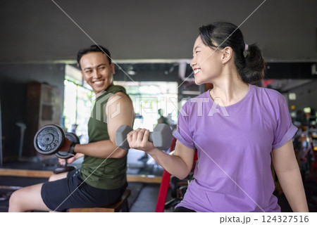Indonesian southeast asian man and chinese east asian woman working out lifting a dumbbell at the gym. Fitness exercise and healthy lifestyle concept 124327516
