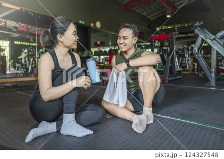 Chinese east asian woman taking a break after exercising with Indonesian southeast asian personal trainer man at the gym. Fitness exercise and healthy lifestyle concept 124327548