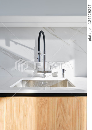 Modern kitchen sink design with sleek flexible faucet and natural wood cabinetry Modern kitchen sink design with sleek flexible faucet and natural wood cabinetry 124329297