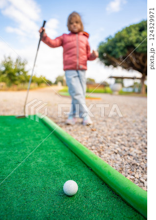 Little girl playing mini golf outdoor. Child having fun with new activity in spring time. Family vacations or resort. 124329971