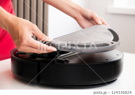 woman cleaning and installing water container in robot vacuum cleaner. housewife in red dress preparing vacuum cleaner before cleaning or cleaning it from dust and debris after cleaning house woman cleaning and installing water container in robot vacuum cleaner. housewife in red dress preparing vacuum cleaner before cleaning or cleaning it from dust and debris after cleaning house 124330824