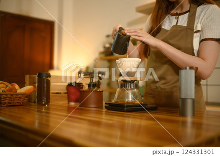 Close up of woman carefully pouring hot water into dripper to make fresh pour over coffee in a home kitchen 124331301