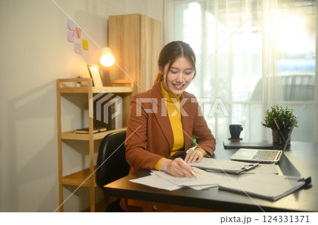 Smiling businesswoman sitting at desk with laptop, reviewing graphs and statistics 124331371