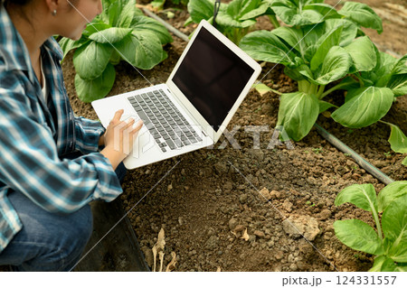Female farmer using laptop in a greenhouse, collecting data and observing plant growth 124331557