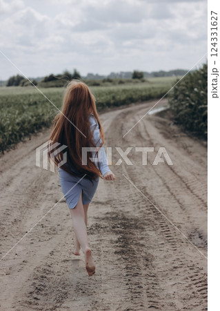 Pretty girl with a hat in her hand walks in a field with field flowers and smiles sincerely. 124331627