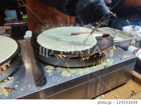 Frying pancakes. Person chef spreading liquid batter on round frying pan spatula. Cooking food on street. Festivities festival. Street food fried batter dough. Vertical 124331639