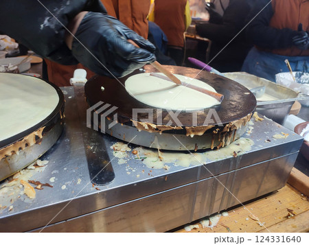 Frying pancakes. Person chef spreading liquid batter on round frying pan spatula. Cooking food on street. Festivities festival. Street food fried batter dough. Vertical 124331640