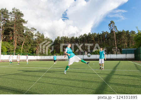 A group of football players are playing on a field. One player kicks the ball while the others watch 124331895