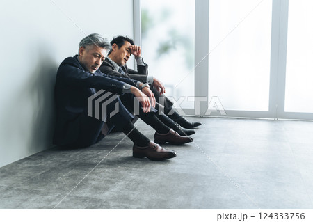 オフィスの床に座り込む二人組のミドルエイジ男性ビジネスパーソン オフィスの床に座り込む二人組のミドルエイジ男性ビジネスパーソン 124333756