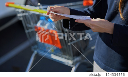 Buyer checks. Customer hold receipt bill. Shopping cart on background. Paper receipt on shopping supermarket. Expensive total. Cash register. Money spending on Hypermarket. Family budget. Check bill. 124334556