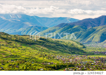 mountainous countryside landscape with kolochava village in the valley. cloudy weather. rural fields and meadows on the forested slopes of a hill. rolling alpine scenery in spring mountainous countryside landscape with kolochava village in the valley. cloudy weather. rural fields and meadows on the forested slopes of a hill. rolling alpine scenery in spring 124334827