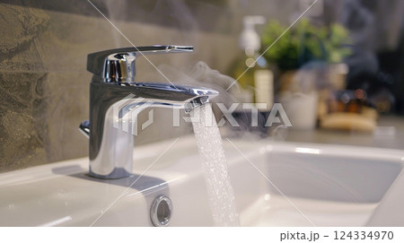 a modern bathroom sink with a chrome faucet from which water and steam come out 124334970