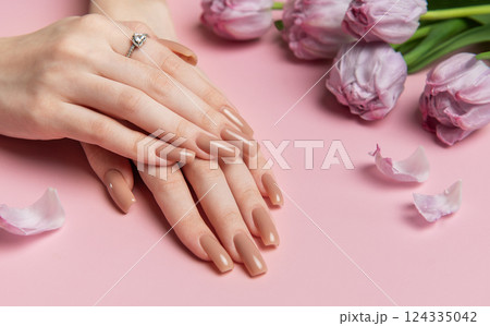 Woman showing stylish nude manicure near pink tulips on pink background 124335042