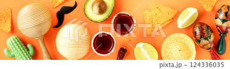 A vibrant Cinco de Mayo-inspired flat lay featuring a sombrero, maracas, tequila shots, lime, chili peppers, nacho chips on a bright yellow and orange backdrop A vibrant Cinco de Mayo-inspired flat lay featuring a sombrero, maracas, tequila shots, lime, chili peppers, nacho chips on a bright yellow and orange backdrop 124336035