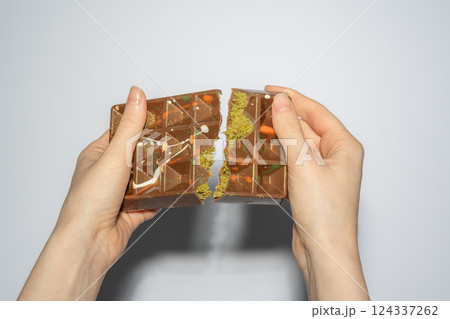 Famous Dubai chocolate with pistachio, tahini and kadaif broken in woman's hands. Confectionery handmade sweets, chocolatier 124337262