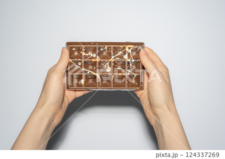 Trend Dubai chocolate with pistachio, tahini and kadaif in woman's hands on white background. Confectionery handmade sweets, chocolatier Trend Dubai chocolate with pistachio, tahini and kadaif in woman's hands on white background. Confectionery handmade sweets, chocolatier 124337269