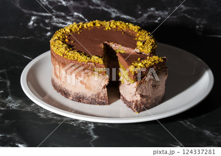 Sliced chocolate Dubai cheesecake with pistachio paste and kataifi dough filling covered in chocolate ganache on white plate. Black background. Indulgence, gourmet desserts, art of culinary Sliced chocolate Dubai cheesecake with pistachio paste and kataifi dough filling covered in chocolate ganache on white plate. Black background. Indulgence, gourmet desserts, art of culinary 124337281