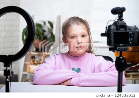 A beautiful blonde teenager is broadcasting live. The video blogger has a live broadcast. An annular lamp and a camera during a live broadcast of a video blogger 124338012