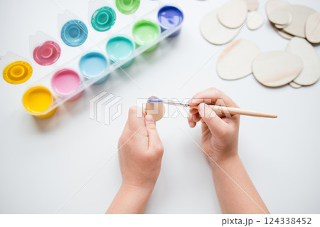 Child painting Esater wooden egg shapes with colorful palette on white table Child painting Esater wooden egg shapes with colorful palette on white table 124338452