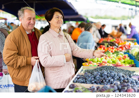 Elderly man and woman buying plums at an open market 124341620
