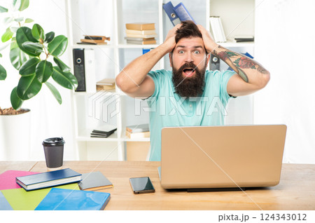 Surprised man with jaw dropped clutching head sitting at laptop in office, surprise Surprised man with jaw dropped clutching head sitting at laptop in office, surprise 124343012