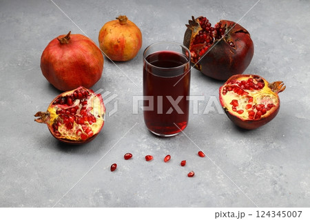 Freshly squeezed pomegranate juice in a glass transparent bottle, broken pomegranate and pomegranate seeds on a black flat stone plate on a dark wooden background top view. Freshly squeezed pomegranate juice in a glass transparent bottle, broken pomegranate and pomegranate seeds on a black flat stone plate on a dark wooden background top view. 124345007