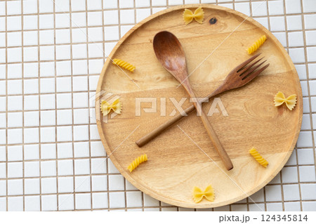 time to eat pasta. wooden plate with fork and spoon in form of clock hands. pasta on plate. time to eat pasta. wooden plate with fork and spoon in form of clock hands. pasta on plate. 124345814