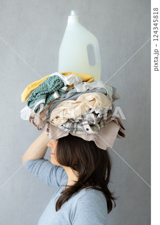 washing clothes, woman holds stack of clothes on head and conditioner laundry after dry cleaning. washing clothes, woman holds stack of clothes on head and conditioner laundry after dry cleaning. 124345818