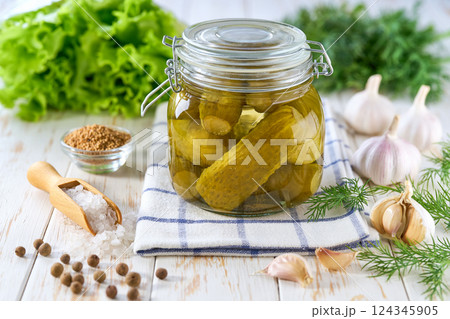 Glass jar of pickled cucumbers and ingredients on wooden table. Marinated cucumbers gherkins. Pickles with dill, salt and garlic. 124345905