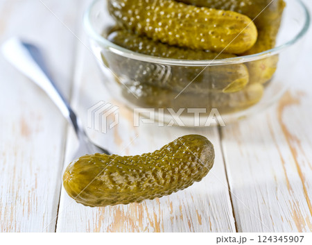 marinated gherkins in a clear glass bowl on a white kitchen table, selective focus. 124345907