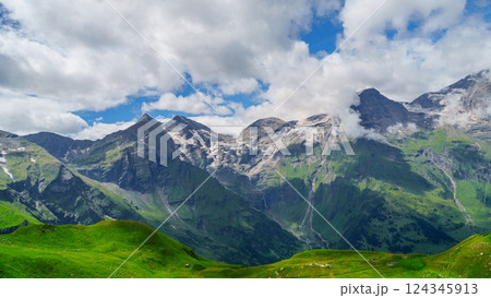 Green mountains with snow-covered peaks and a blue sky with white clouds Green mountains with snow-covered peaks and a blue sky with white clouds 124345913