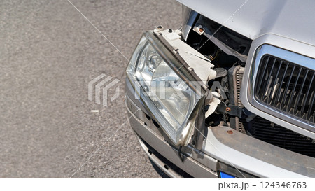 Crashed car, detail on front headlight, glass not broken, hanging from dented bumper plates Crashed car, detail on front headlight, glass not broken, hanging from dented bumper plates 124346763