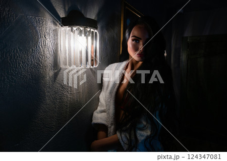 Woman posing in elegant lingerie beside soft light in a dimly lit room 124347081