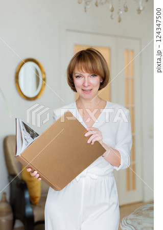 An adult beautiful woman spends time in her stylish living room and holds a big book in her hands. 124347500