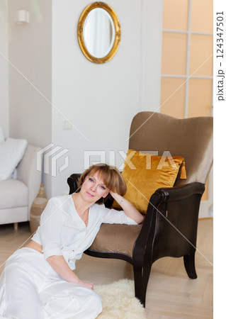Calm peaceful adult homeowner woman resting and sitting on the floor at comfort stylish living room. 124347501