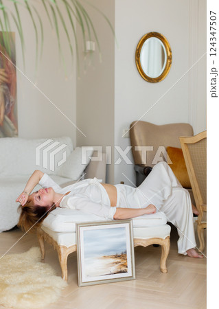 A woman is lying on a sofa in a stylish, bright living room next to a beautiful picture she painted herself. 124347507