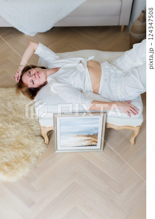 A woman is lying on a sofa in a stylish, bright living room next to a beautiful picture she painted herself. 124347508