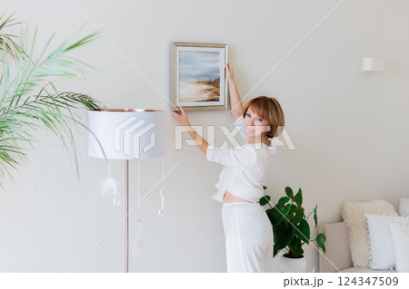 Woman hanging picture on wall in room. Interior design. 124347509