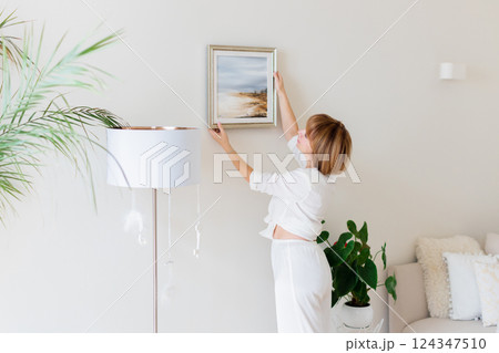 Woman hanging picture on wall in room. Interior design. 124347510
