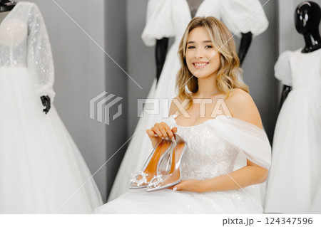 The bride-to-be is wearing a wedding dress at a fitting in the salon, choosing shoes for the wedding 124347596