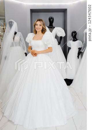 Pretty young woman is choosing a wedding dress in the shop. The bride-to-be is wearing a wedding dress for fitting 124347602