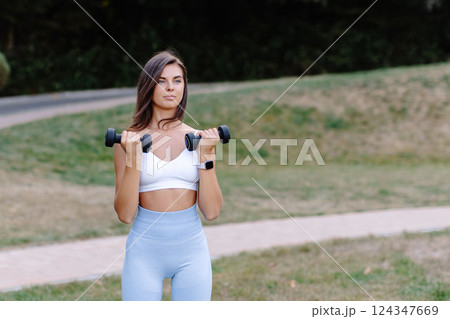 Young woman lifting weights during outdoor workout in a park Young woman lifting weights during outdoor workout in a park 124347669