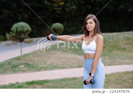 Young woman exercising with dumbbells in a park 124347670