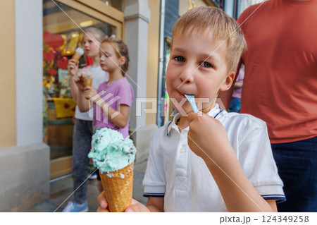 Portrait cute cheerful child enjoy ice cream walk together with family at european city street road on hot summer sunny day. Funny kids eat sweet vanilla icecream walking outdoors Portrait cute cheerful child enjoy ice cream walk together with family at european city street road on hot summer sunny day. Funny kids eat sweet vanilla icecream walking outdoors 124349258